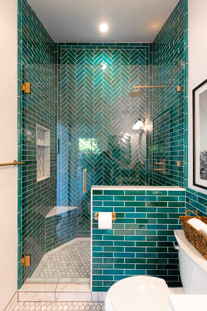 Luxury bathroom with teal herringbone tile shower and gold fixtures